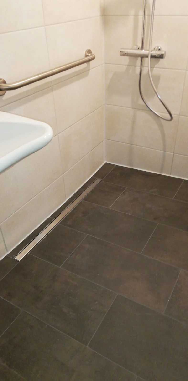Bodengleiche Dusche mit Edelstahl-Duschrinne und Haltegriff im rollstuhlgerechten Bad
