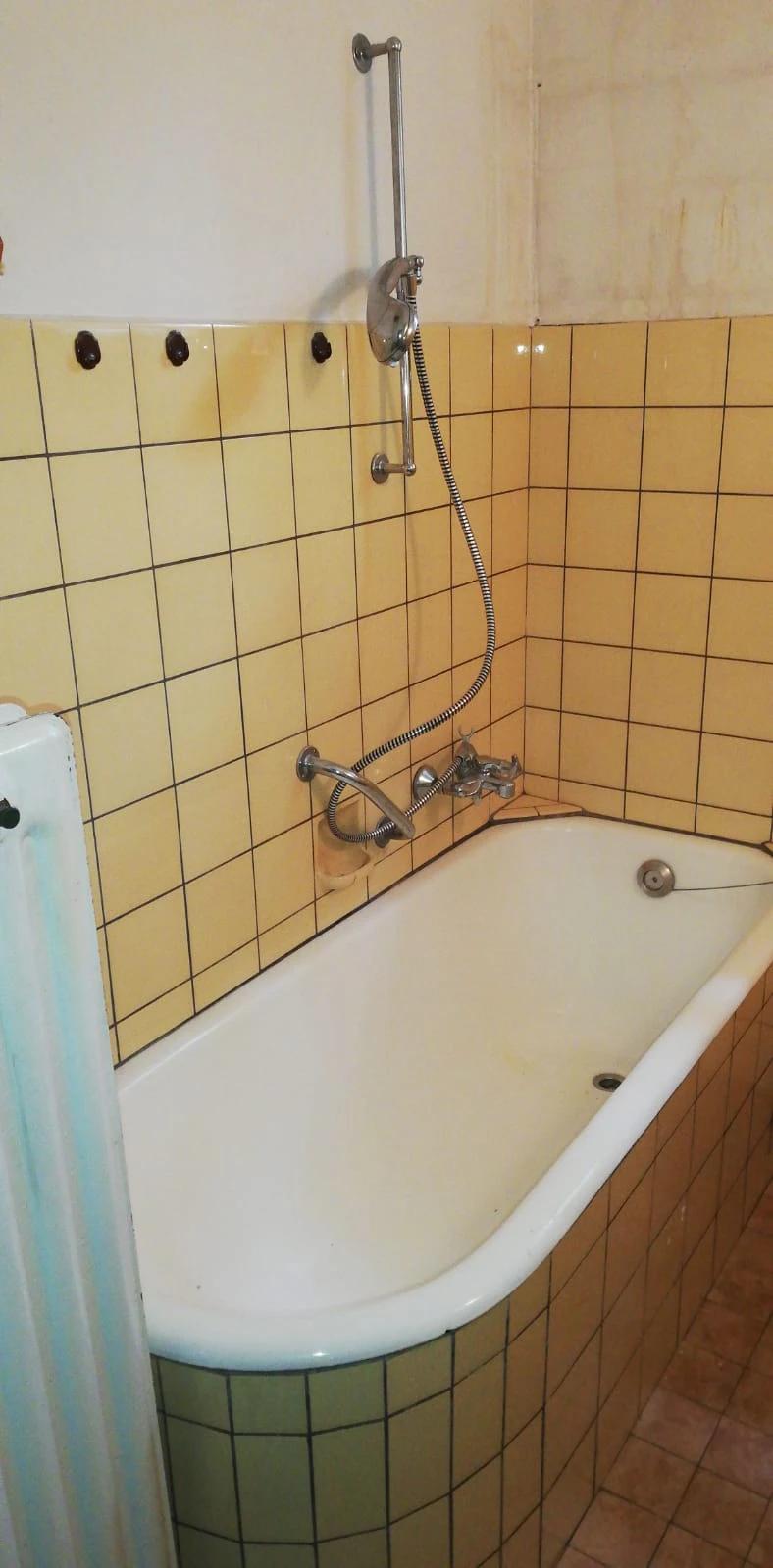 Alte, hohe Badewanne mit gelben und grünen Fliesen